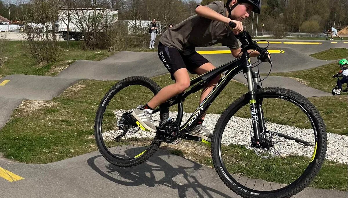 Kind macht Wheelie auf Pumptrack – Helm, Balance und Spaß auf kurviger Strecke mit gelben Pfeilen. | © DAV Markt Schwaben | Foto Miron Thoms