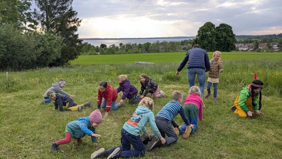 Eine Gruppe von Kindern spielt fröhlich mit einem Erwachsenen auf einer grünen Wiese. Sie bewegen sich aktiv und genießen die gemeinsame Zeit. | © DAV Markt Schwaben | Foto: Familiengruppe