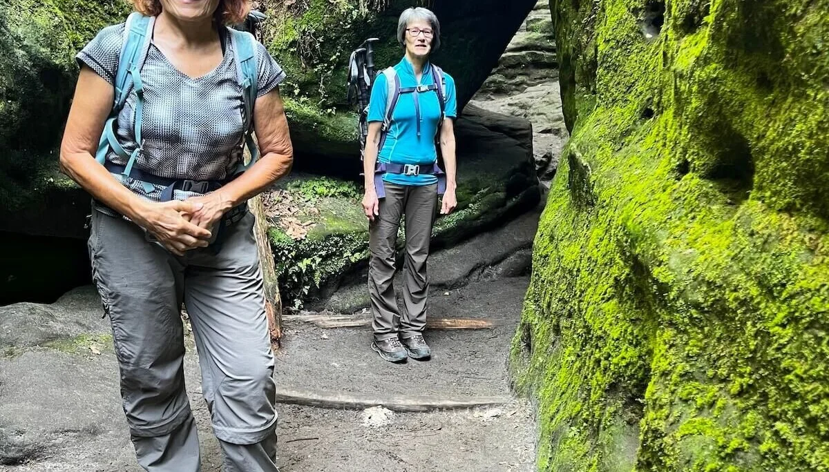 Zwei Personen stehen auf Steinpfad zwischen moosbedeckten Felsen, umgeben von Farnen und dichter Vegetation. | © DAV Markt Schwaben | Foto Edith Zerrle
