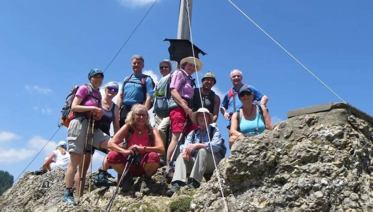 Wandergruppe am Gipfelkreuz des Bärenköpfle bei Sonnenschein, umgeben von Felsen und blauem Himmel, nach erfolgreichem Aufstieg. | © DAV Markt Schwaben
