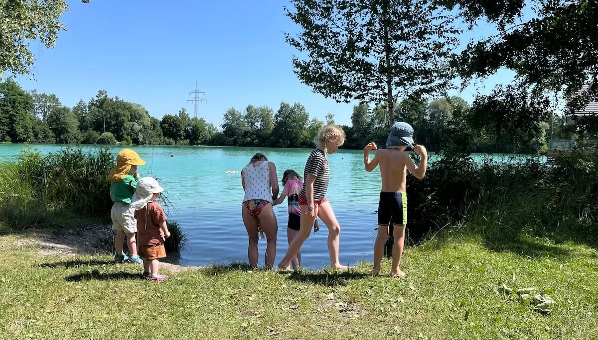 Kinder stehen am Ufer des Wiflinger Weihers, genießen die Natur nach einer gemeinsamen Radtour – ein sommerliches Familienabenteuer. | © DAV Markt Schwaben | Foto: Lara Wolff