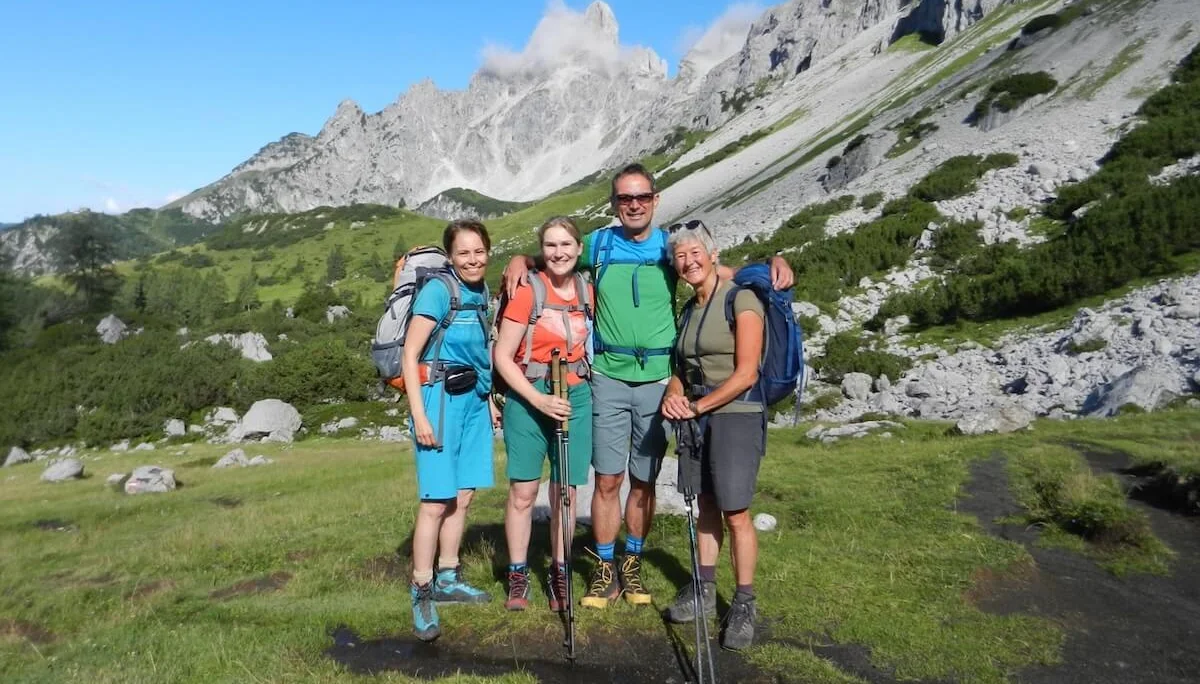 Vier Wandernde posieren in alpiner Kulisse mit Blick auf die Bischofsmütze – grüne Hügel, Fels und Wolken umrunden den Gipfel. | © DAV Markt Schwaben | Foto: Christine Strasser