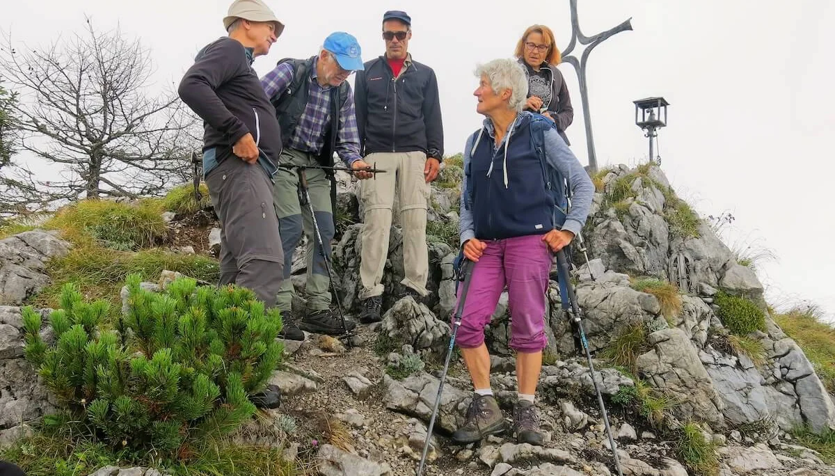 Fünf Bergsteiger stehen am felsigen Gipfel mit Kreuz und Laterne, im Vordergrund Ausrüstung und Gespräch. | © DAV Markt Schwaben · Foto: Erwin Matzinger