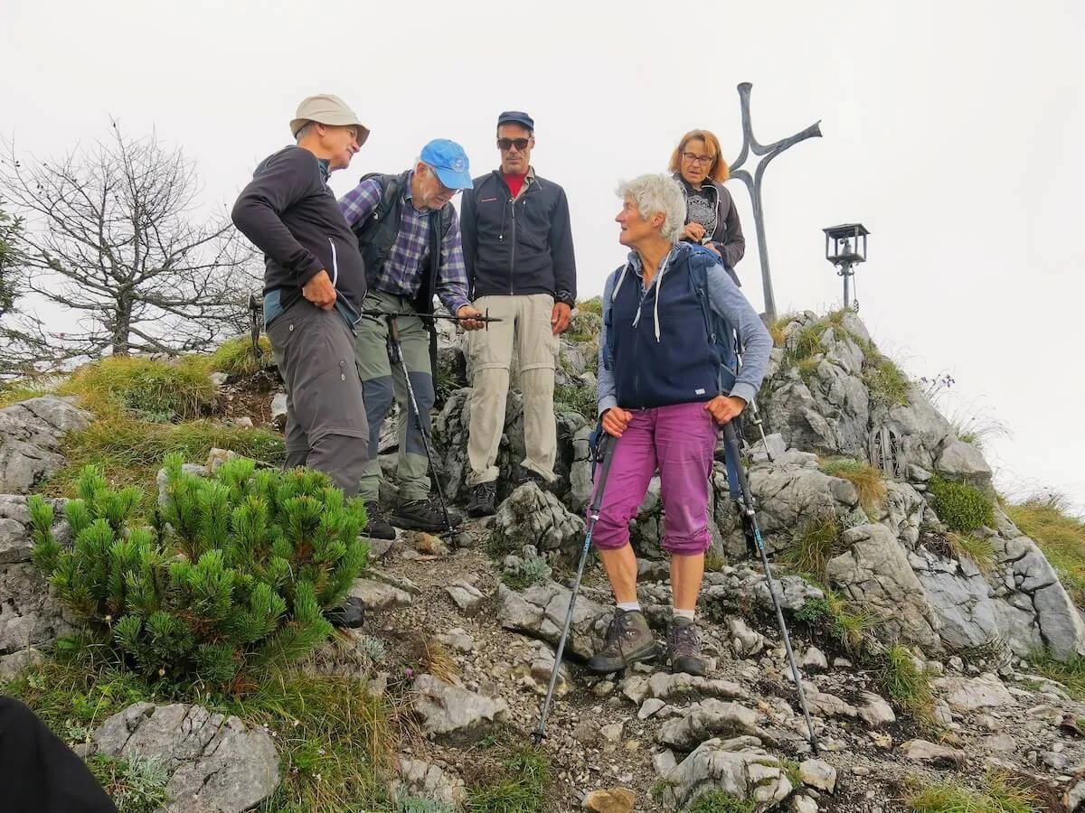 Fünf Bergsteiger stehen am felsigen Gipfel mit Kreuz und Laterne, im Vordergrund Ausrüstung und Gespräch. | © DAV Markt Schwaben · Foto: Erwin Matzinger