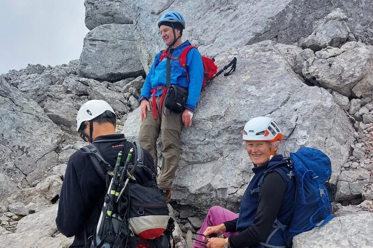 Drei Bergsteiger rasten auf felsigem Grat, einer sitzt lächelnd, hinten steiles Gelände und Waldhang. | © DAV Markt Schwaben · Foto: Lutz Gründel