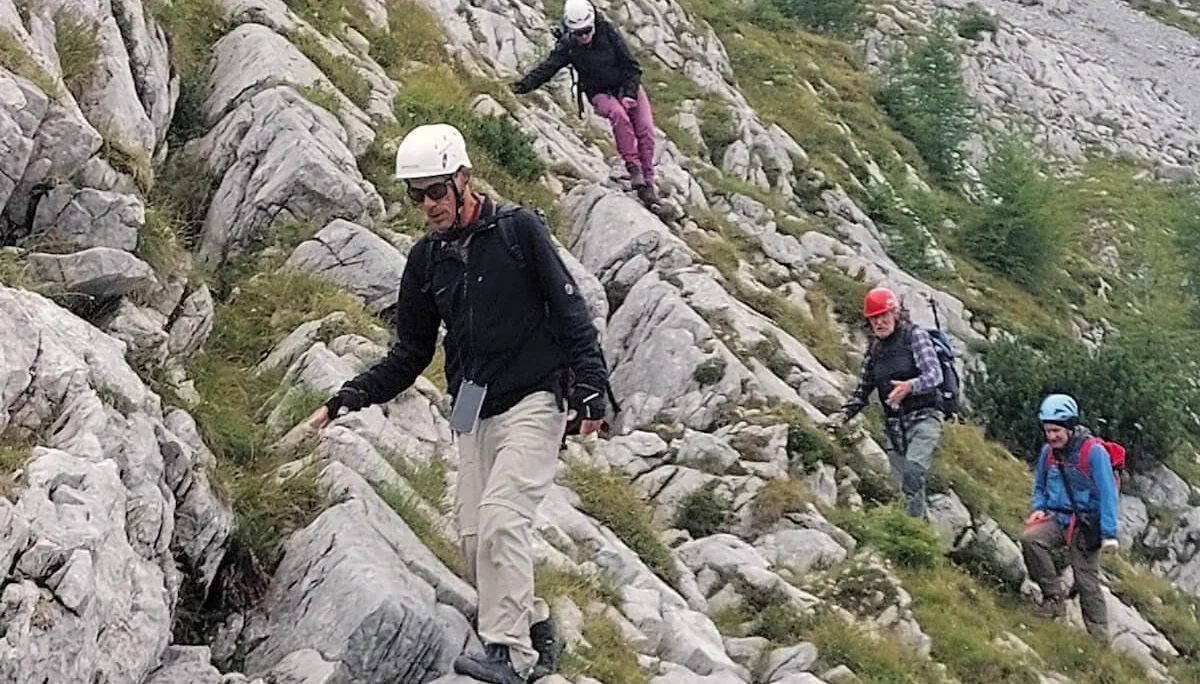 Vier Bergsteiger steigen über felsiges Gelände mit Grasinseln ab, im Hintergrund steiler Bergwald. | © DAV Markt Schwaben · Foto: Lutz Gründel