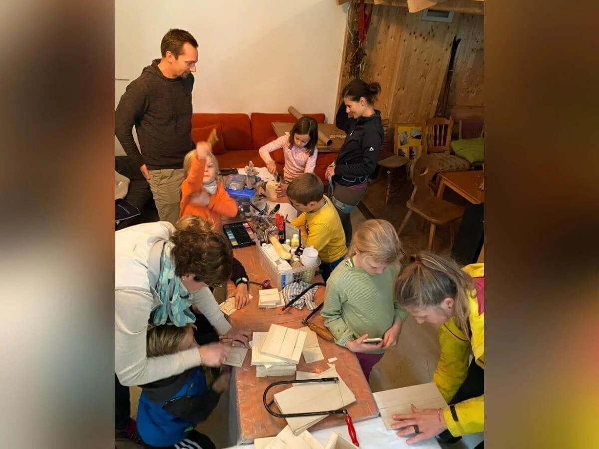 Kinder und Erwachsene gestalten am Basteltisch farbenfrohe Holzobjekte; im Hintergrund ein Holzspielhaus. | © DAV Markt Schwaben | Foto: Helena De Monte
