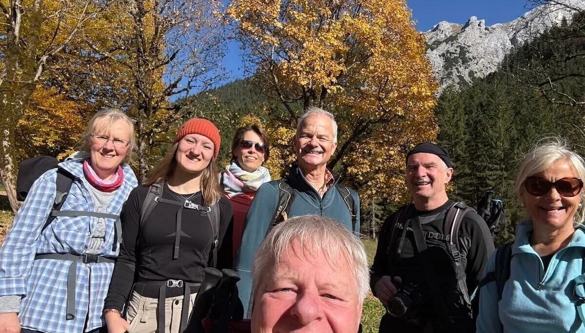 Sieben Erwachsene stehen vor herbstlich gefärbten Bäumen und Berggipfeln, lächeln in Wanderausrüstung in die Kamera. | © DAV Markt Schwaben · Foto: Markus Zimmermann