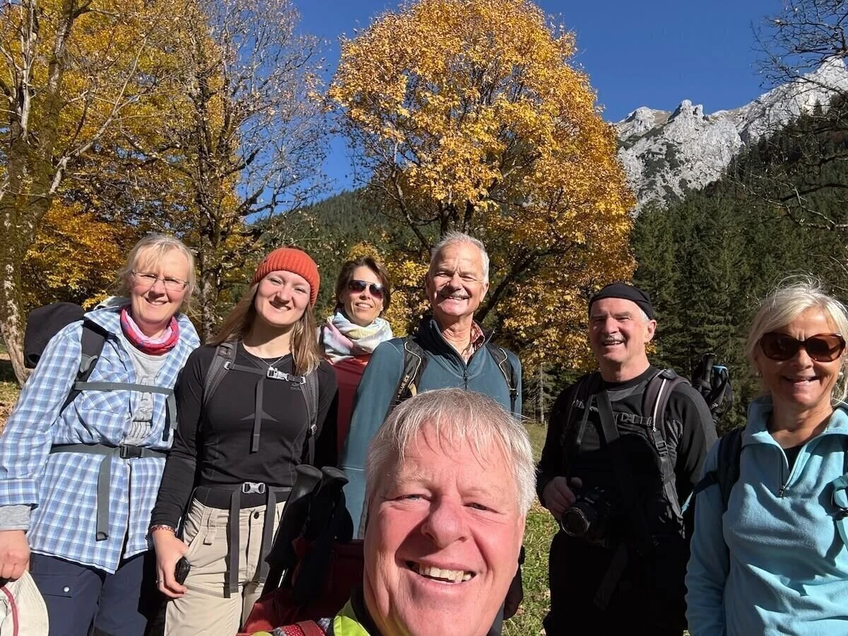 Sieben Erwachsene stehen vor herbstlich gefärbten Bäumen und Berggipfeln, lächeln in Wanderausrüstung in die Kamera. | © DAV Markt Schwaben · Foto: Markus Zimmermann
