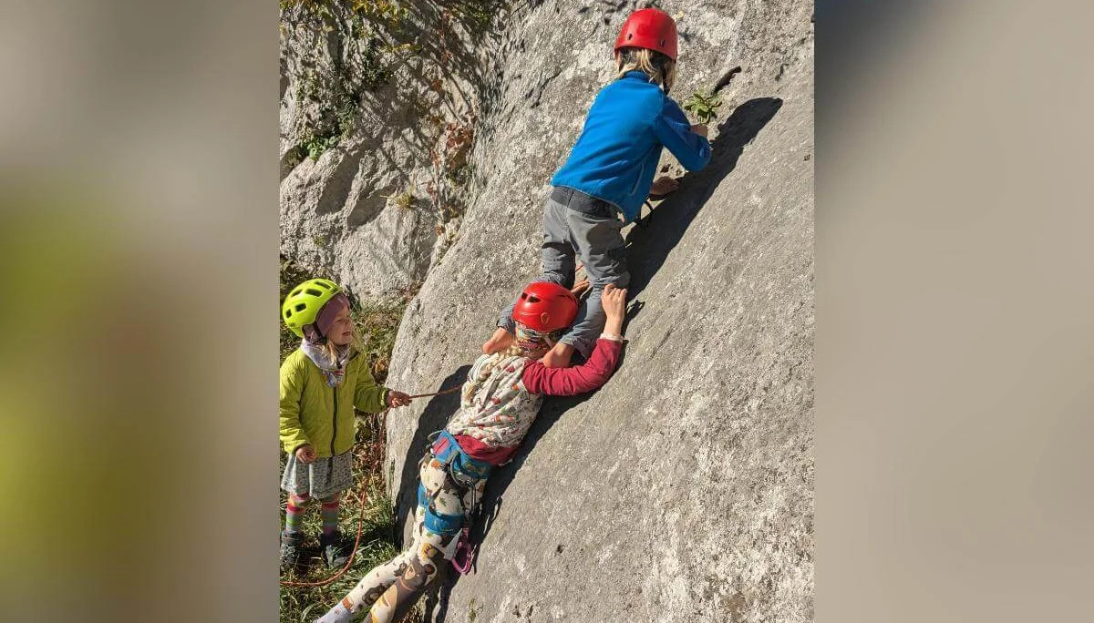 Mehrere Kinder stehen auf einer Wiese und füttern zwei schwarze Ziegen mit grünen Blättern. Einige tragen Helme. Im Hintergrund sind Bäume, Felsen und Sonnenlicht zu sehen. | © DAV Markt Schwaben · Foto: Silke Titze