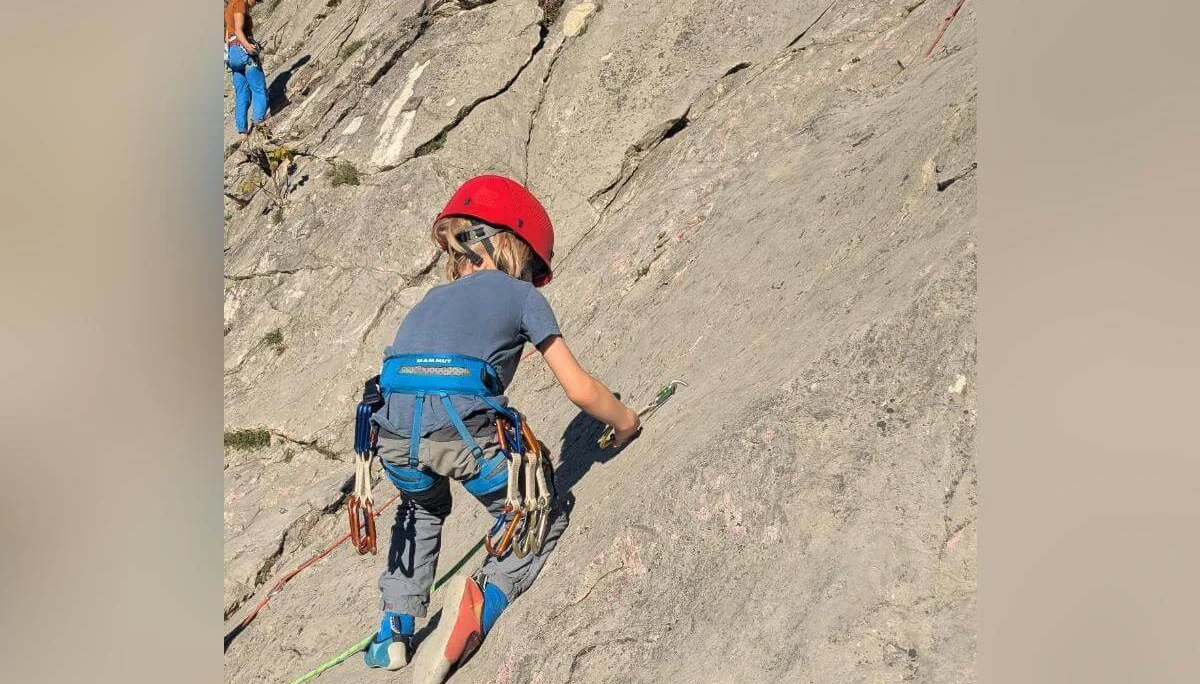 Zwei Kinder mit Helmen stehen auf einer Wiese vor einem Felsen und hantieren gemeinsam mit einem Kletterseil. Im Hintergrund sind ein Weinberg, Herbstlaub und eine felsige Landschaft zu sehen. | © DAV Markt Schwaben · Foto: Silke Titze