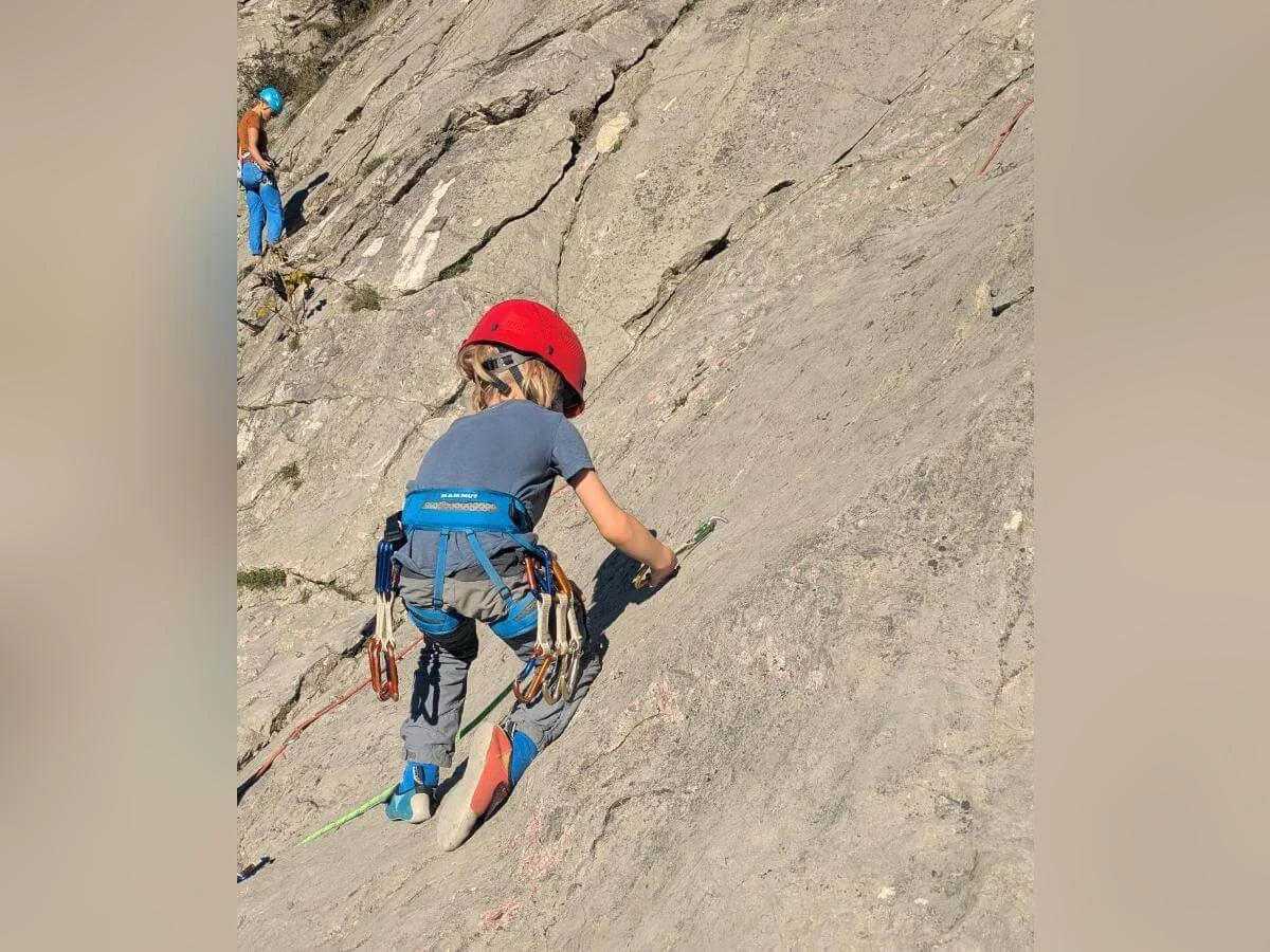 Zwei Kinder mit Helmen stehen auf einer Wiese vor einem Felsen und hantieren gemeinsam mit einem Kletterseil. Im Hintergrund sind ein Weinberg, Herbstlaub und eine felsige Landschaft zu sehen. | © DAV Markt Schwaben · Foto: Silke Titze