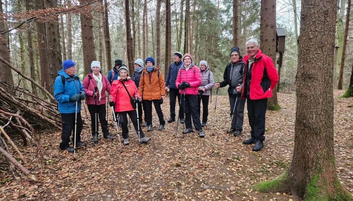 Zwölf Senioren stehen in Winterkleidung auf einem Laubweg im Wald, im Hintergrund hohe Bäume und Aststruktur. | © DAV Markt Schwaben · Foto: Hubert Inhofer