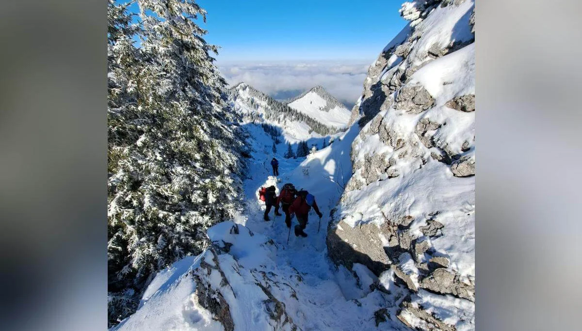Wandergruppe steigt durch verschneites Gelände mit Blick auf ferne Berggipfel über Wolken, Felsen und Bäume flankieren den Pfad. | © DAV Markt Schwaben · Foto Tanja Döhler