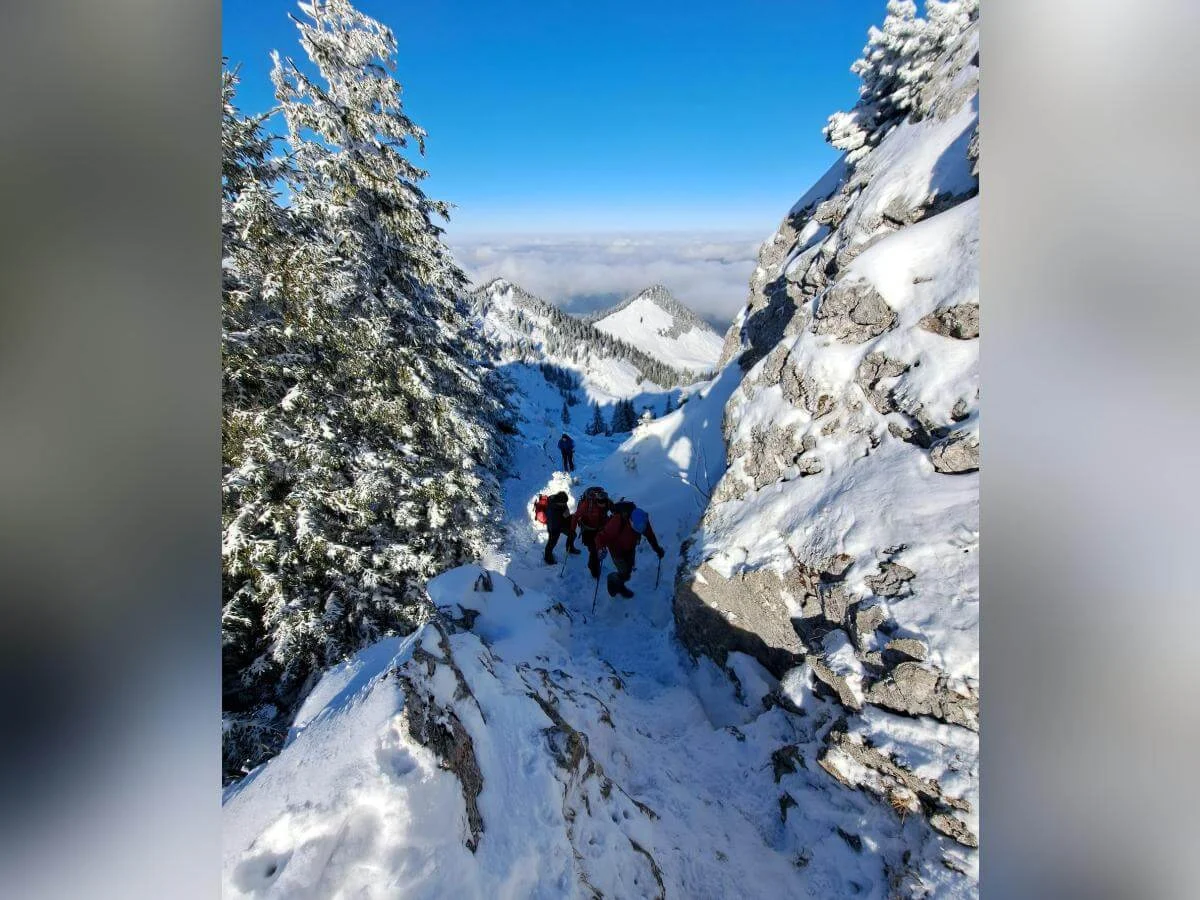 Wandergruppe steigt durch verschneites Gelände mit Blick auf ferne Berggipfel über Wolken, Felsen und Bäume flankieren den Pfad. | © DAV Markt Schwaben · Foto Tanja Döhler
