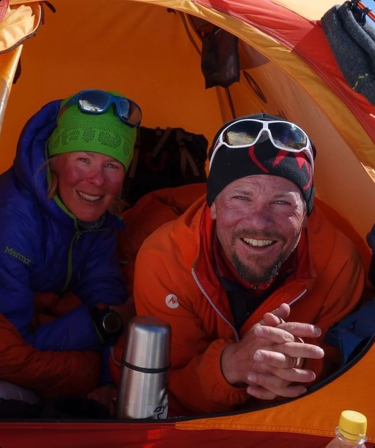 Zwei Personen sitzen in einem orangefarbenen Zelt auf einem verschneiten Berg, tragen Winterausrüstung und Sonnenbrillen. | © Alix von Melle