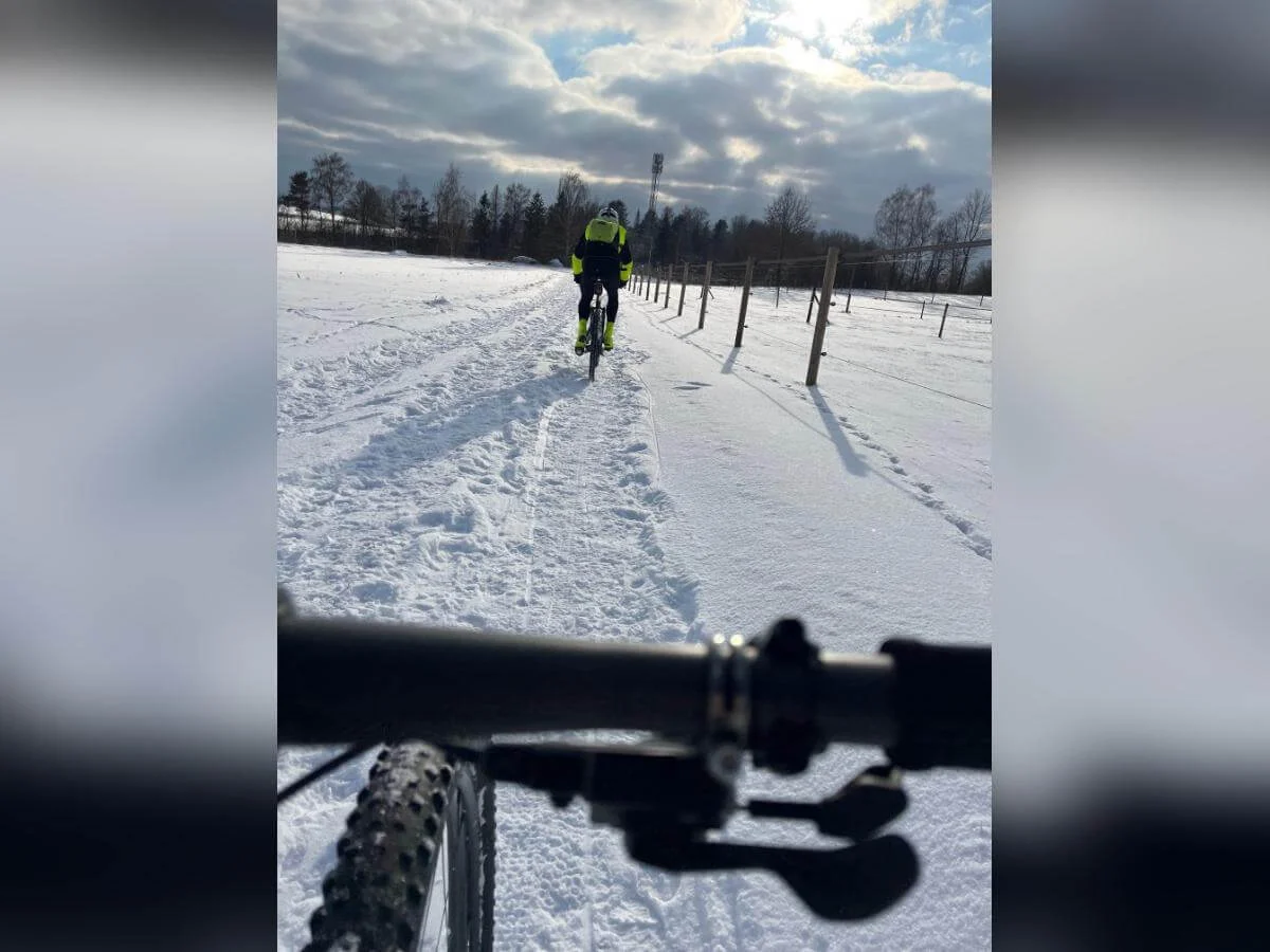 Lenker im Vordergrund, ein Radfahrer voraus auf verschneitem Weg; Zaunpfähle und Bäume rahmen die winterliche Szene. | © DAV Markt Schwaben | Foto: Miron Thoms
