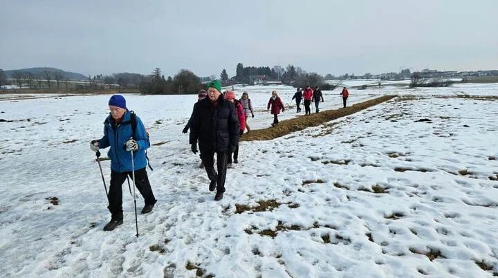 Seniorinnen und Senioren wandern auf einem schmalen Weg durch verschneite Felder; im Hintergrund stehen Bäume und einzelne Gebäude. | © DAV Markt Schwaben | Foto: Hubert Inhofer