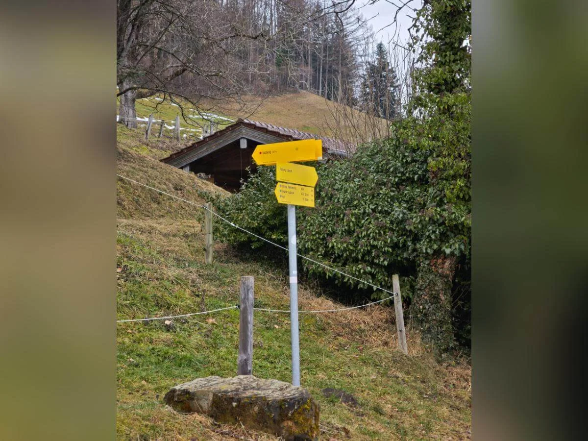 Gelber Wegweiser im Vordergrund vor einer kleinen Holzhütte und einem bewaldeten Hang; die Schilder zeigen verschiedene Wanderziele. | © DAV Markt Schwaben | Foto: Erwin Matzinger