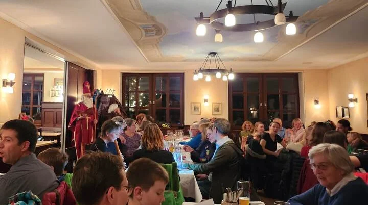 Festlich geschmückter Raum mit geselligen Gästen bei der Weihnachtsfeier des DAV Markt Schwaben 2025. Warme Beleuchtung, fröhliche Atmosphäre und traditionelle Weihnachtsfiguren im Hintergrund | © DAV Markt Schwaben