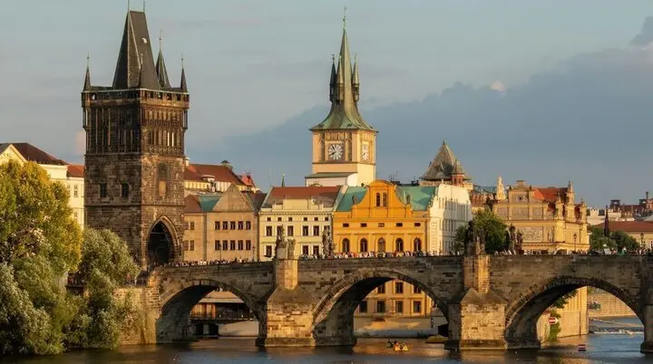 Historische Karlsbrücke in Prag bei Sonnenuntergang, mit gotischen Türmen und barocken Gebäuden im Hintergrund. | © Foto Martin Krchnacek on Unsplash