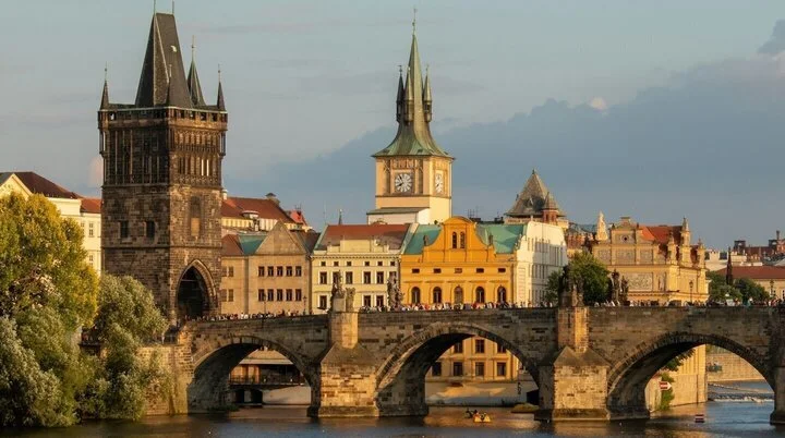 Historische Karlsbrücke in Prag bei Sonnenuntergang, mit gotischen Türmen und barocken Gebäuden im Hintergrund. | © Foto Martin Krchnacek on Unsplash