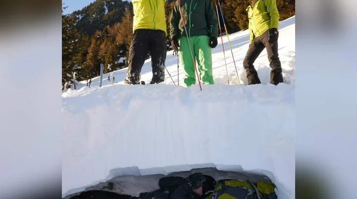 Drei Teilnehmer einer Skitourenausbildung stehen auf einer Schneedecke und sondieren mit Lawinensonden. Unter ihnen liegt eine Person in einer Schneehöhle, ausgerüstet mit Winterkleidung und Rucksack. Die Szene zeigt eine praktische Übung zur Verschüttetensuche im Rahmen der alpinen Ausbildung. | © DAV Markt Schwaben | Foto Markus Sellmeier