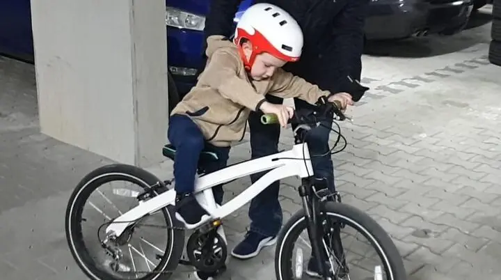 Ein Kind mit Fahrradhelm übt das Fahren auf einem Fahrrad, während ein Erwachsener unterstützend daneben steht. | © DAV Markt Schwaben · Foto: Anna Thoms