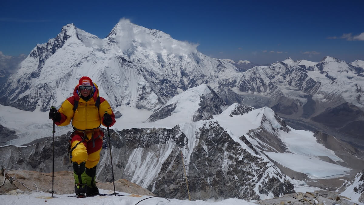 Alix Makalu 2014 Hintergrund Everest | © Alix von Melle Ein Bergsteiger in gelbem und rotem Anzug steht mit Kletterausrüstung auf einem schneebedeckten Bergrücken, umgeben von Gipfeln. | © Alix von Melle