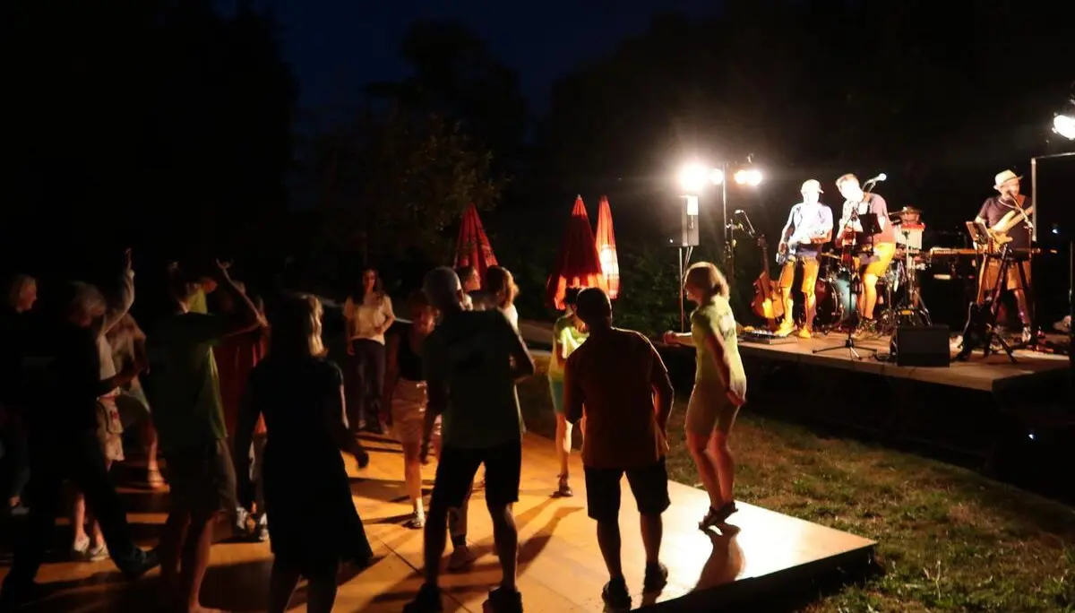 Menschen tanzen abends auf einer Holzplattform vor der beleuchteten Bühne. | © DAV Markt Schwaben/Susanne Mayer