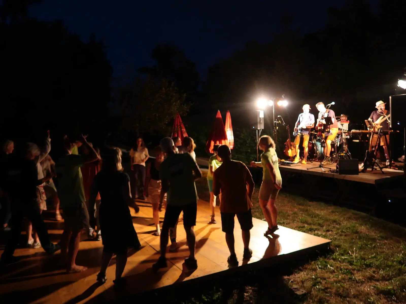 Menschen tanzen abends auf einer Holzplattform vor der beleuchteten Bühne. | © DAV Markt Schwaben/Susanne Mayer
