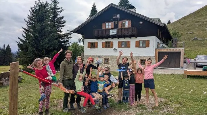 Eine große Gruppe aus Kindern und Erwachsenen steht vor der Schönfeldhütte im Gebirge. Alle lächeln, einige heben die Arme, und die Stimmung wirkt fröhlich und gemeinschaftlich. | © DAV Markt Schwaben · Familiengruppe