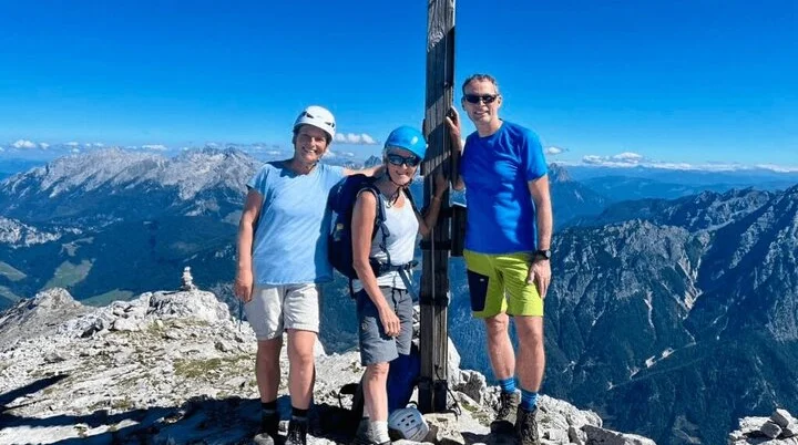 Drei Wanderer auf Berggipfel neben Holzkreuz – klare Sicht, Natur genießen und gemeinsames Abenteuer erleben. | © DAV Markt Schwaben | Foto Markus Sellmeier
