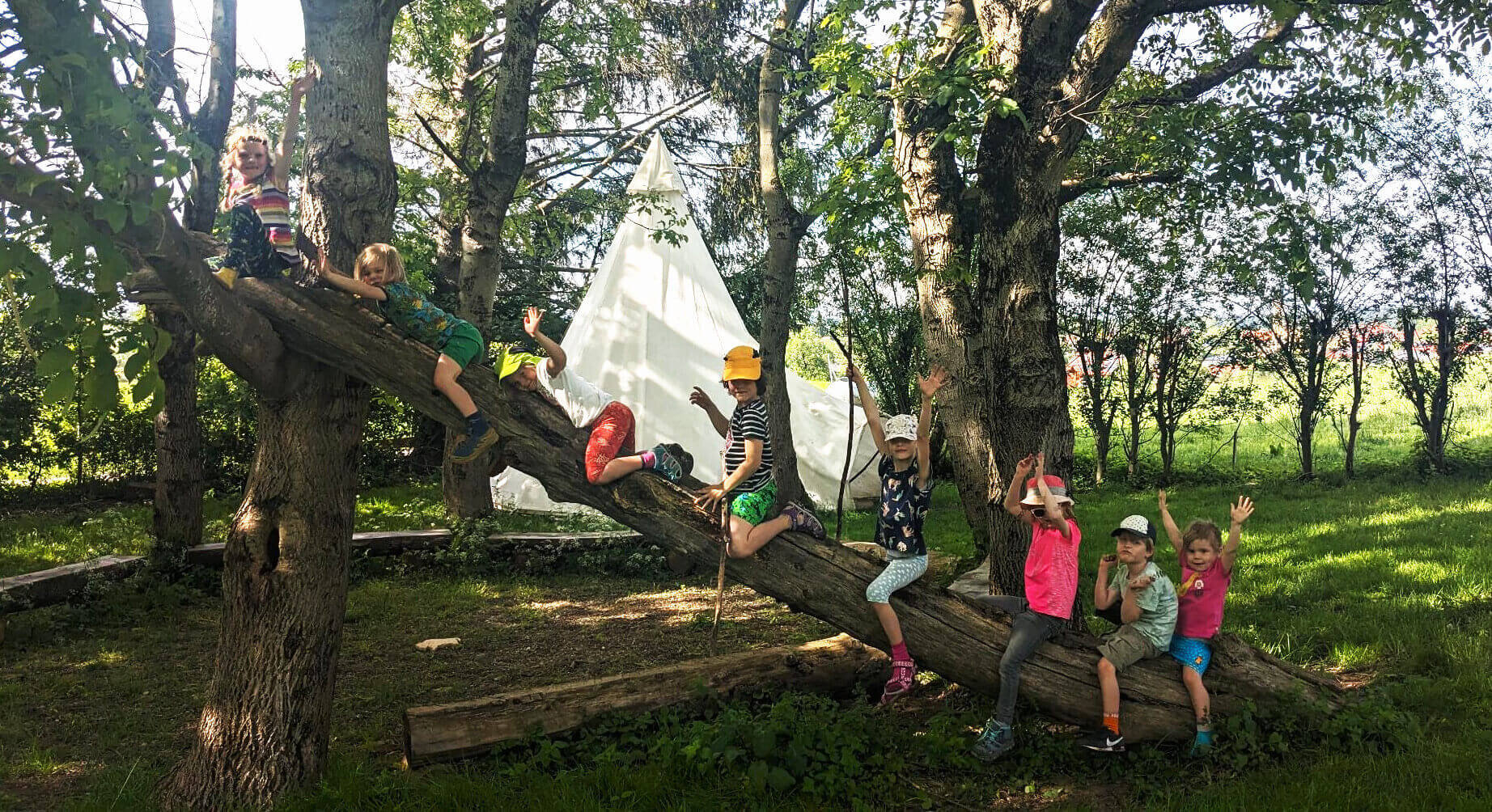 Kinder sitzen fröhlich auf einer Picknickdecke in der Natur und strecken die Arme in die Luft. Umgeben von Rucksäcken und Proviant genießen sie ein gemeinsames Abenteuer – Familiengruppe der DAV-Sektion Markt Schwaben. | © DAV Markt Schwaben