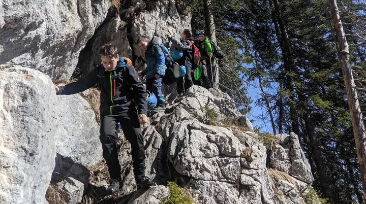 Mehrere Jugendliche steigen mit Rucksäcken über steinigen Bergpfad; Felsblöcke und Kiefern im Hintergrund. | © DAV Markt Schwaben | Foto Florian Kaiser 2024