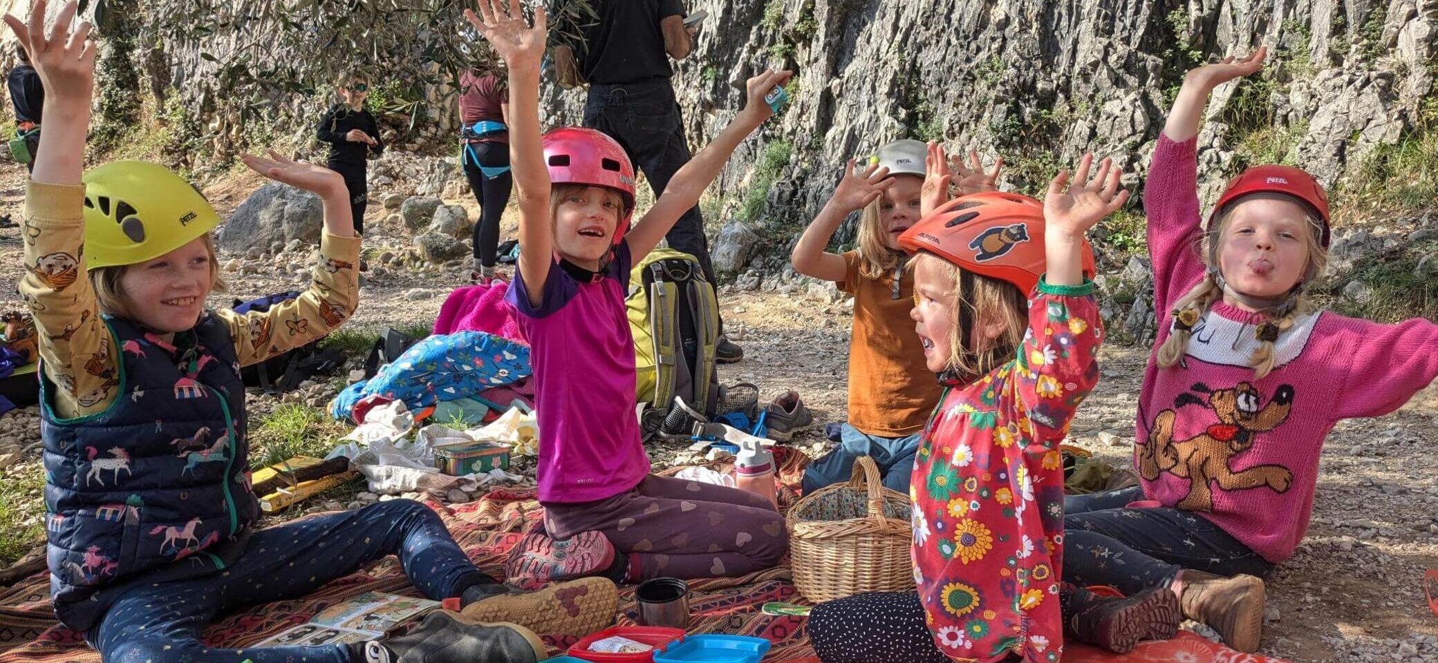 Kinder sitzen fröhlich auf einer Picknickdecke in der Natur und strecken die Arme in die Luft. Umgeben von Rucksäcken und Proviant genießen sie ein gemeinsames Abenteuer – Familiengruppe der DAV-Sektion Markt Schwaben. | © DAV Markt Schwaben | Familiengruppe