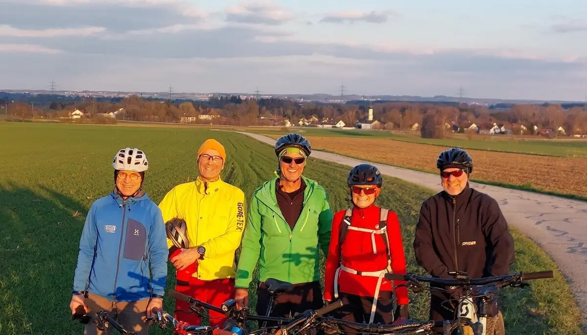 Fünf Radfahrer stehen mit ihren Mountainbikes auf einem Weg zwischen Feldern; im Hintergrund Häuser, Bäume und ein sonniger Himmel. | © DAV Markt Schwaben