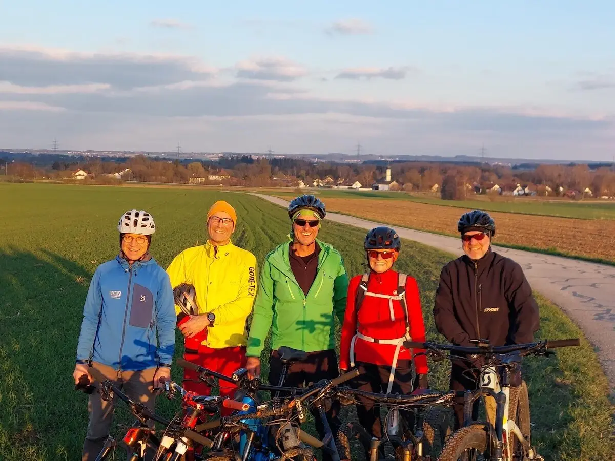 Fünf Radfahrer stehen mit ihren Mountainbikes auf einem Weg zwischen Feldern; im Hintergrund Häuser, Bäume und ein sonniger Himmel. | © DAV Markt Schwaben