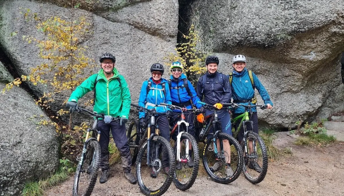 Fünf Radfahrer stehen mit ihren Mountainbikes vor großen Felsen; nasser Boden, herbstliche Bäume und Outdoor‑Szene im Gelände. | © DAV Markt Schwaben