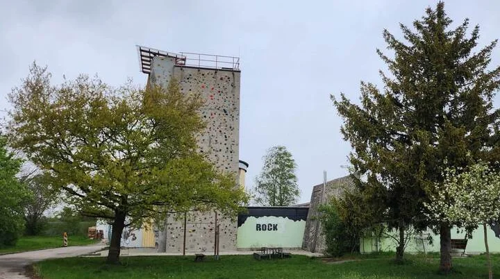 Das Kletterzentrum der DAV-Sektion Markt Schwaben – eine hohe Kletterwand mit bunten Griffen, umgeben von Bäumen und Natur, bietet Herausforderungen für alle Kletterbegeisterten. | © DAV Markt Schwaben