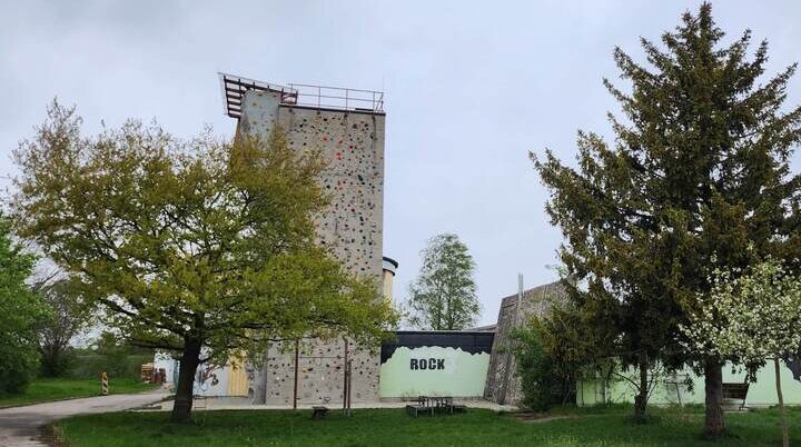 Das Kletterzentrum der DAV-Sektion Markt Schwaben – eine hohe Kletterwand mit bunten Griffen, umgeben von Bäumen und Natur, bietet Herausforderungen für alle Kletterbegeisterten. | © DAV Markt Schwaben