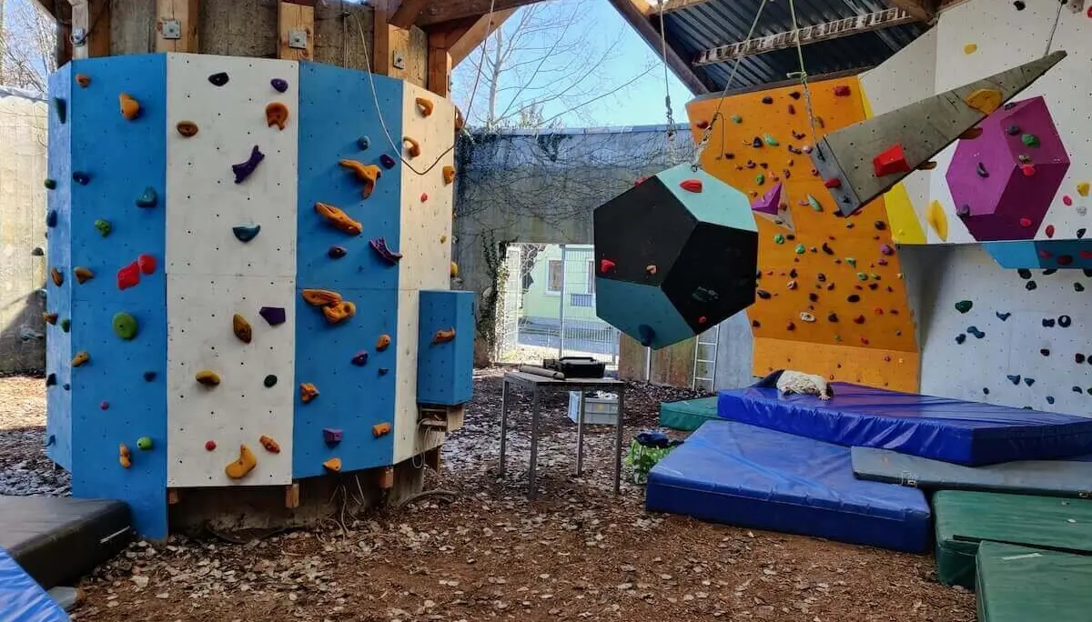 Boulderbereich mit farbigen Griffen, großen Volumen und Matten unter einem Holzdach; vielfältige Kletterstrukturen im Bouldertempel. | © DAV Markt Schwaben/Max Mayer · 2023