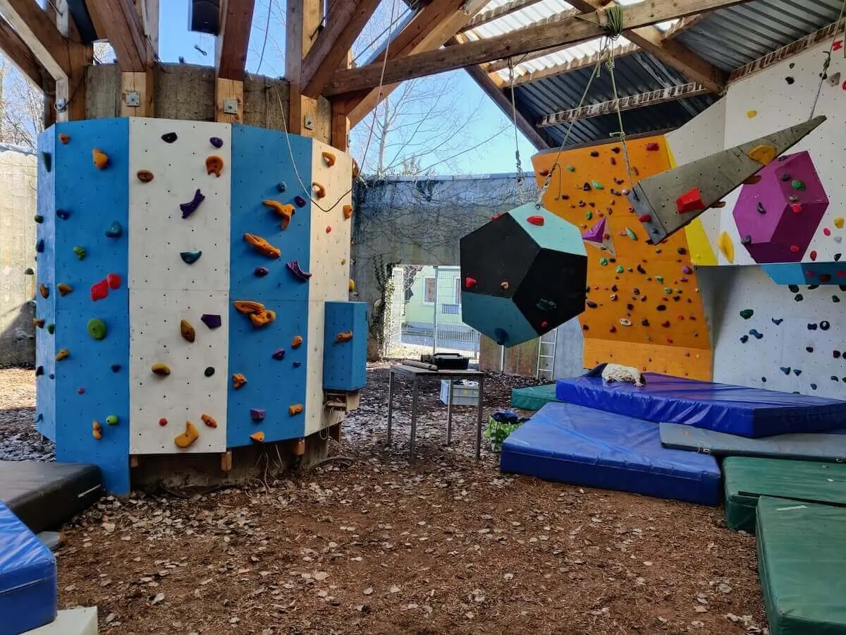 Boulderbereich mit farbigen Griffen, großen Volumen und Matten unter einem Holzdach; vielfältige Kletterstrukturen im Bouldertempel. | © DAV Markt Schwaben/Max Mayer · 2023