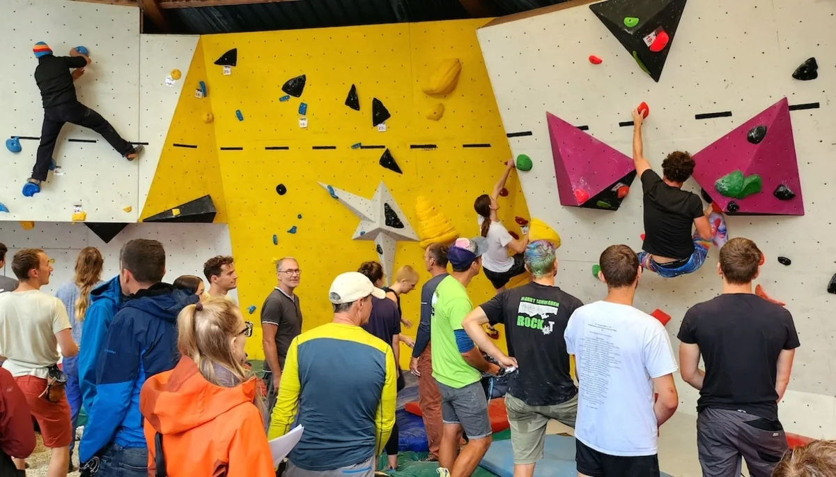 Spannende Wettkämpfe beim Bouldercup | © DAV Markt Schwaben | Foto Anna Thoms Mehrere Kletternde erklimmen die Boulderwand, während Zuschauer gespannt das Geschehen im Kletterzentrum verfolgen. | © DAV Markt Schwaben | Foto Anna Thoms