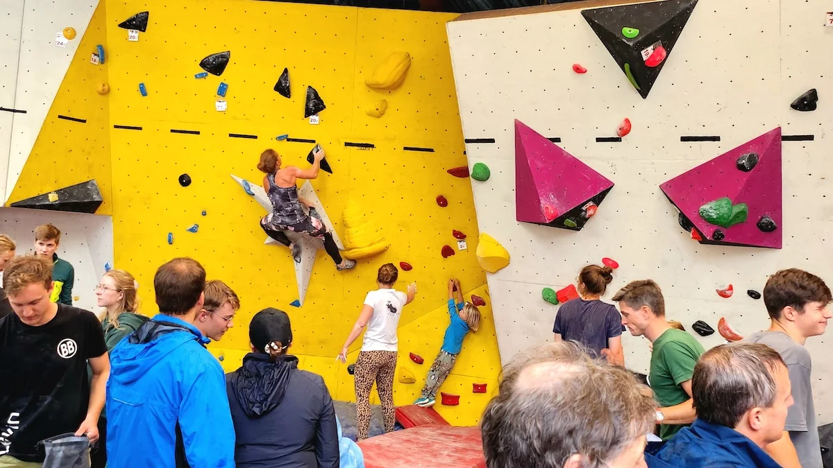 Bouldercup mit Rekordzahl | © DAV Markt Schwaben | Foto Anna Thoms Junge und erwachsene Kletternde zeigen ihr Können an bunten Boulderwänden – Publikum beobachtet gespannt das Geschehen. | © DAV Markt Schwaben | Foto Anna Thoms
