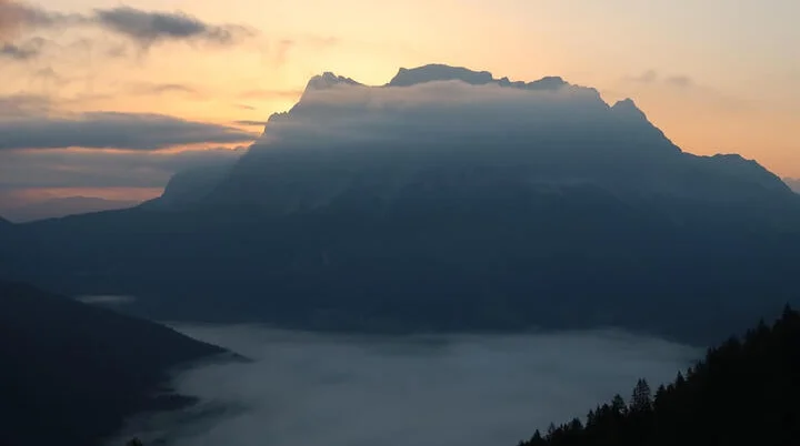 Nebelverhüllte Berggipfel bei Sonnenaufgang, davor ein dichter Wald. | © DAV Markt Schwaben | Foto Susanne Mayerl
