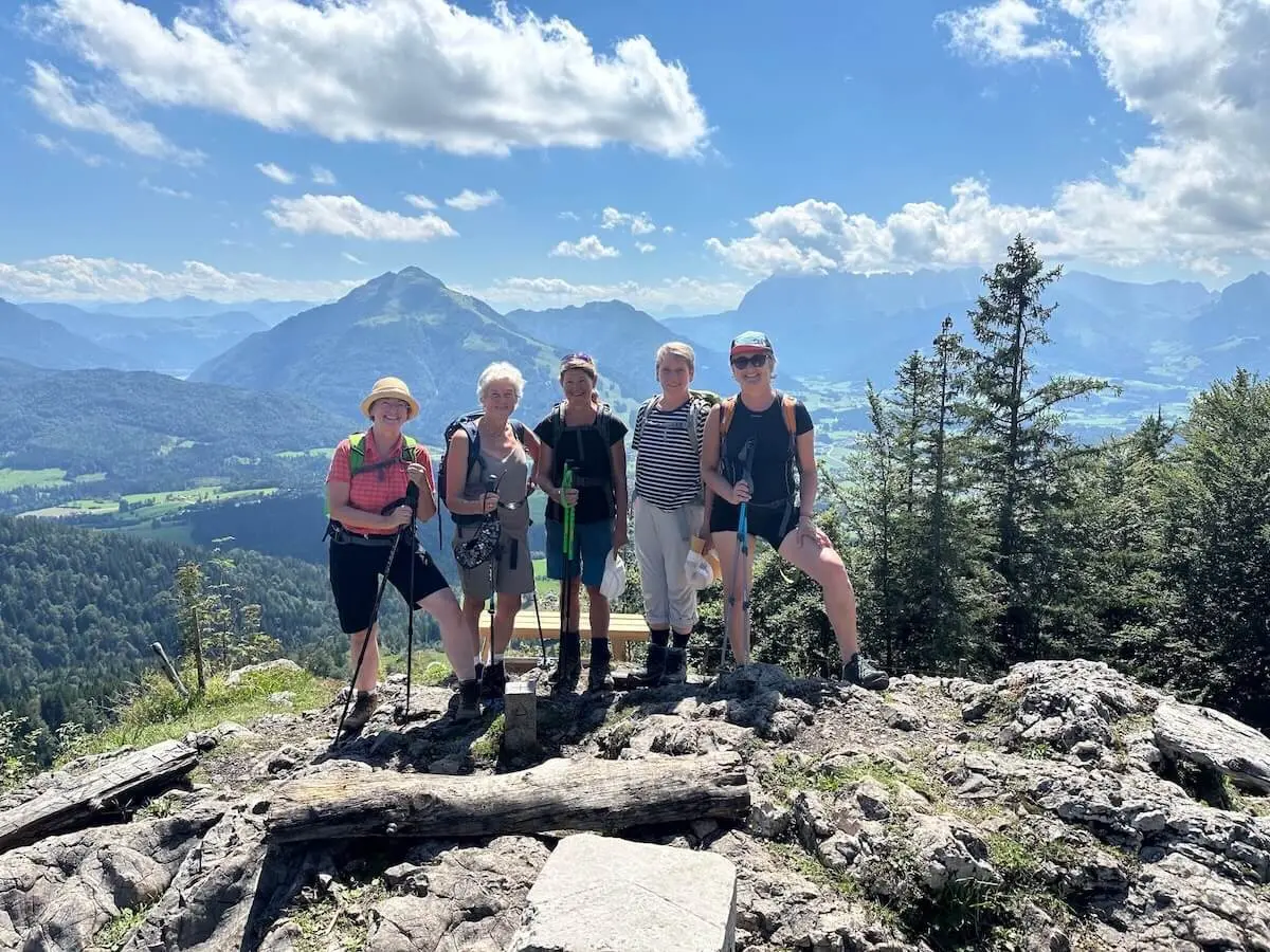 Eine Gruppe von fünf Wanderern steht auf einem felsigen Aussichtspunkt mit Wanderstöcken, umgeben von einer beeindruckenden Berglandschaft mit grünen Tälern und bewaldeten Hängen. Die klare Luft und die weite Aussicht symbolisieren Abenteuer, Gemeinschaft und die Freude am Wandern – Jetzt Mitglied werden und Teil des Alpenvereins werden! | © DAV Markt Schwaben/Elke Kressirer