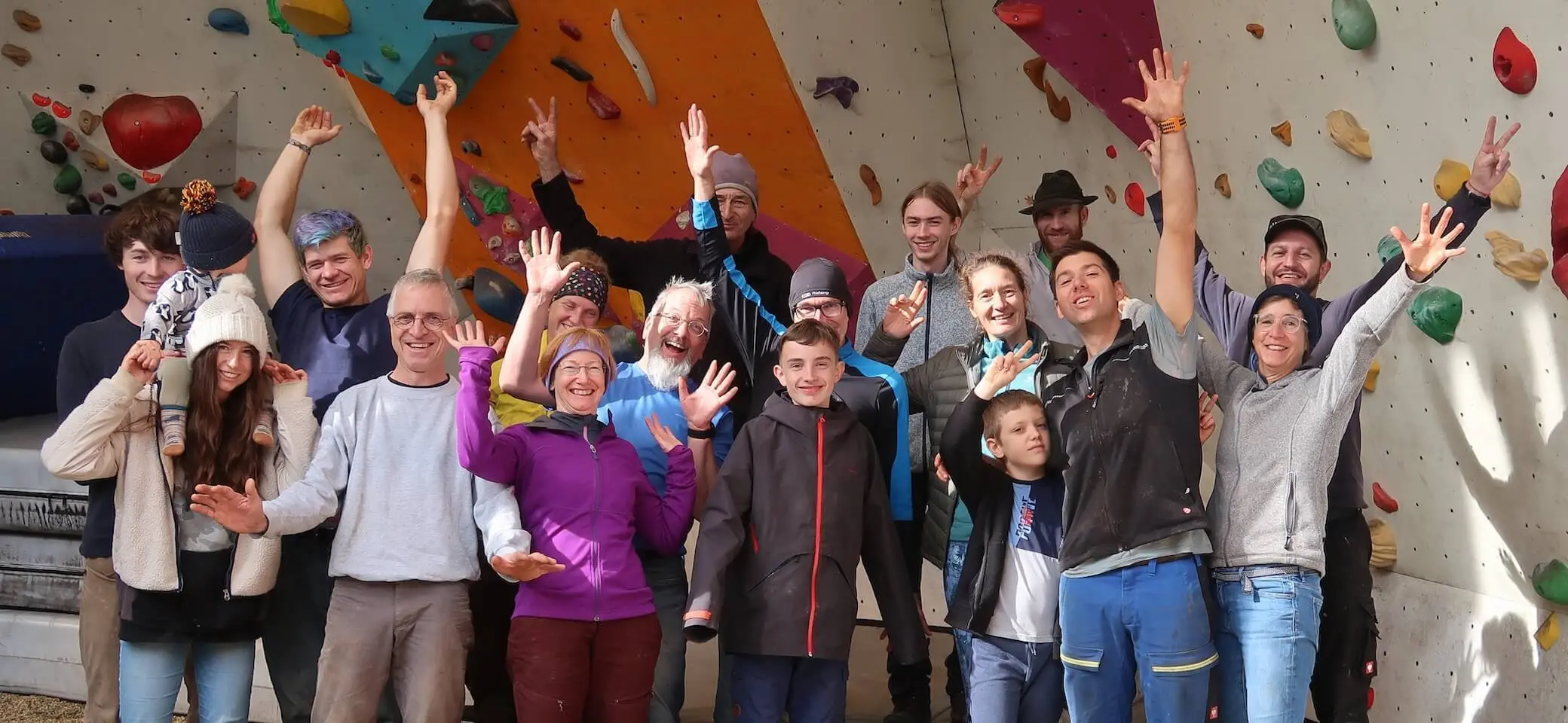 Gruppe von Ehrenamtlichen steht vor einer Indoor‑Kletterwand und hebt jubelnd die Hände; gemeinsames Teamfoto im Kletterzentrum. | © DAV Markt Schwaben