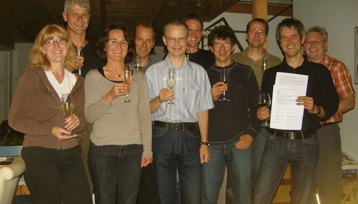 Zehn Personen stehen zusammen in einem Raum und stoßen mit Sektgläsern an. Eine Person hält ein Dokument mit Text und Unterschriften. Die Szene wirkt feierlich, möglicherweise im Zusammenhang mit einer Vertragsunterzeichnung. | © DAV Markt Schwaben