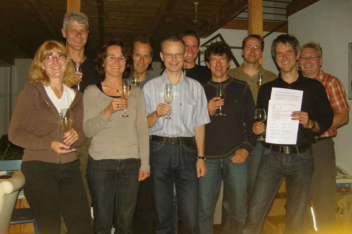 Zehn Personen stehen zusammen in einem Raum und stoßen mit Sektgläsern an. Eine Person hält ein Dokument mit Text und Unterschriften. Die Szene wirkt feierlich, möglicherweise im Zusammenhang mit einer Vertragsunterzeichnung. | © DAV Markt Schwaben